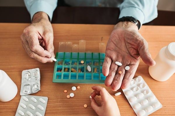 Man's hand holds pills while surrounded by packets of other medications 414048050