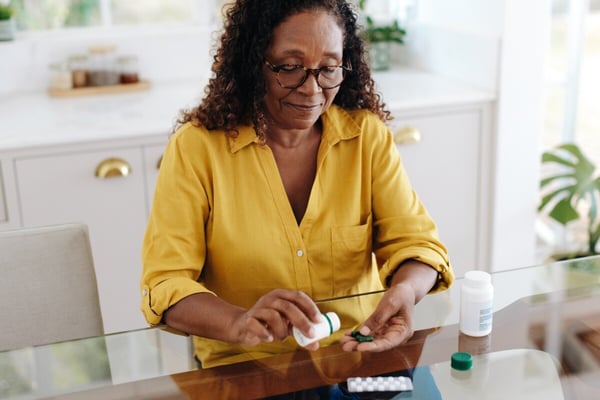 Older Black woman dispenses medication at home 600720024