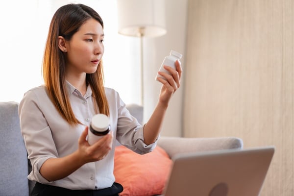 Woman examines pharmaceutical bottles while seating in front of a laptop 639064152