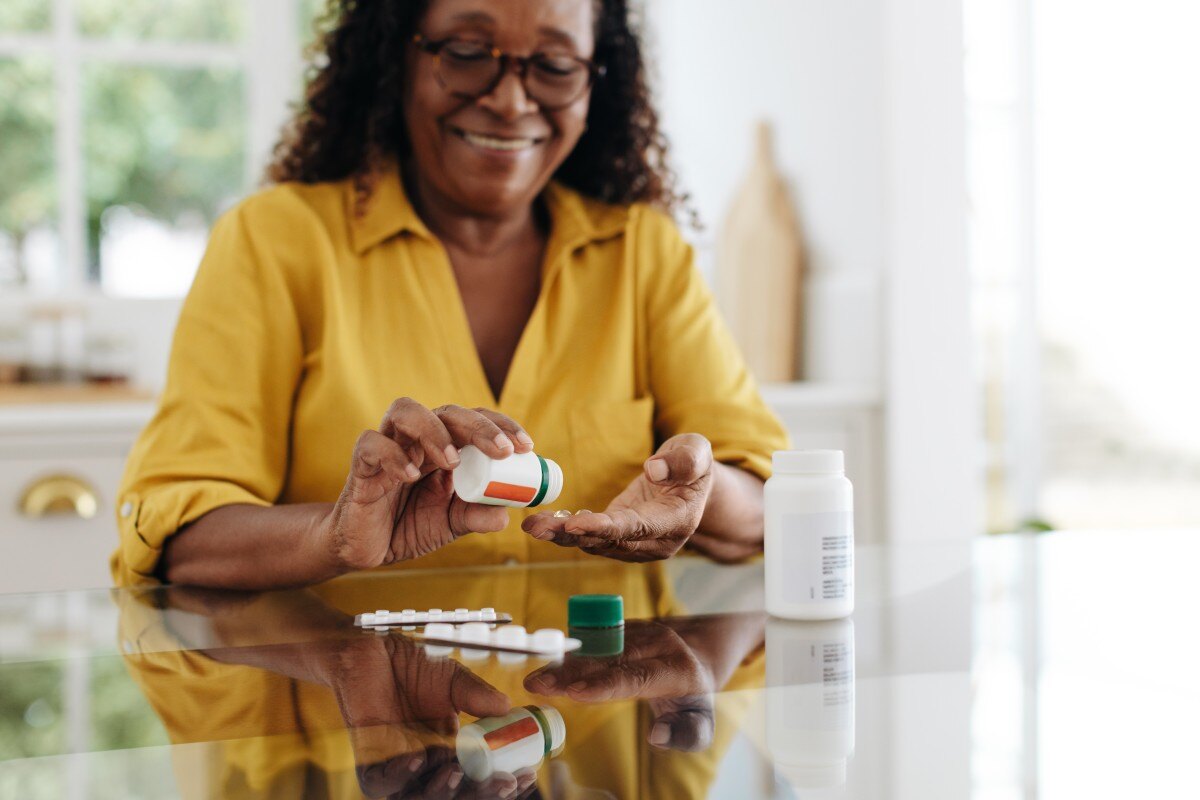 Older Black woman shakes pill bottle into hand to take medication 670965635