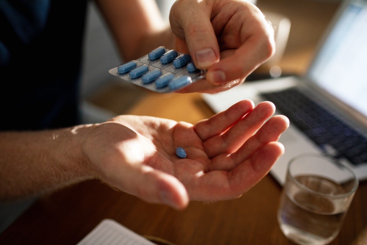 man's hand with pill and laptop in background 683529876