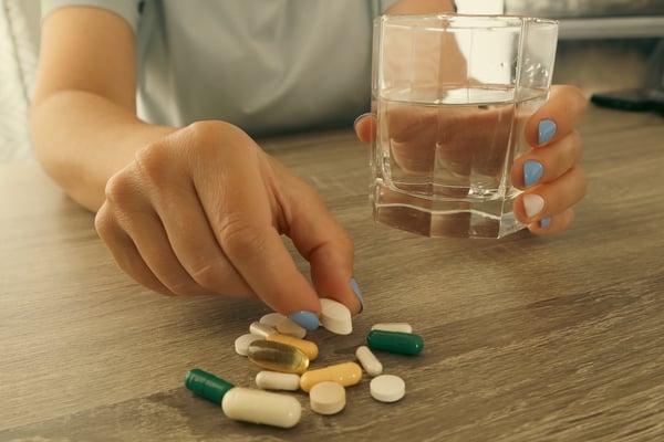 person holding a glass and reaching for medication regimen on table