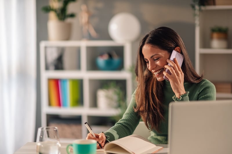 smiling remote pharmacist speaking on a cell phone with a patient and taking notes on interaction
